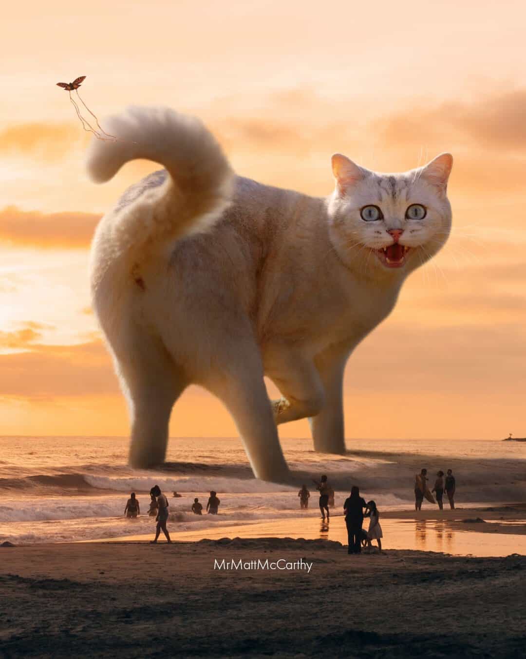 Giant cat on beach at sunset with people and kite in background.
