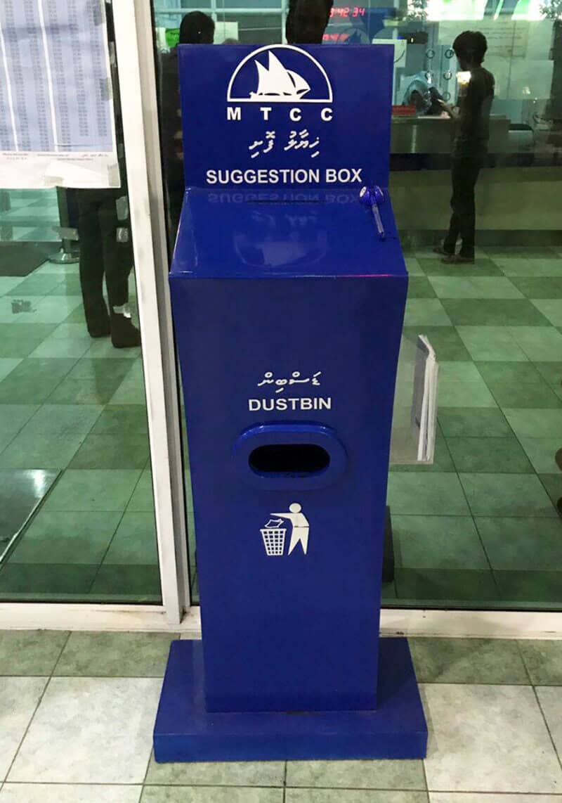 Blue suggestion box with dustbin label and trash icon at airport.