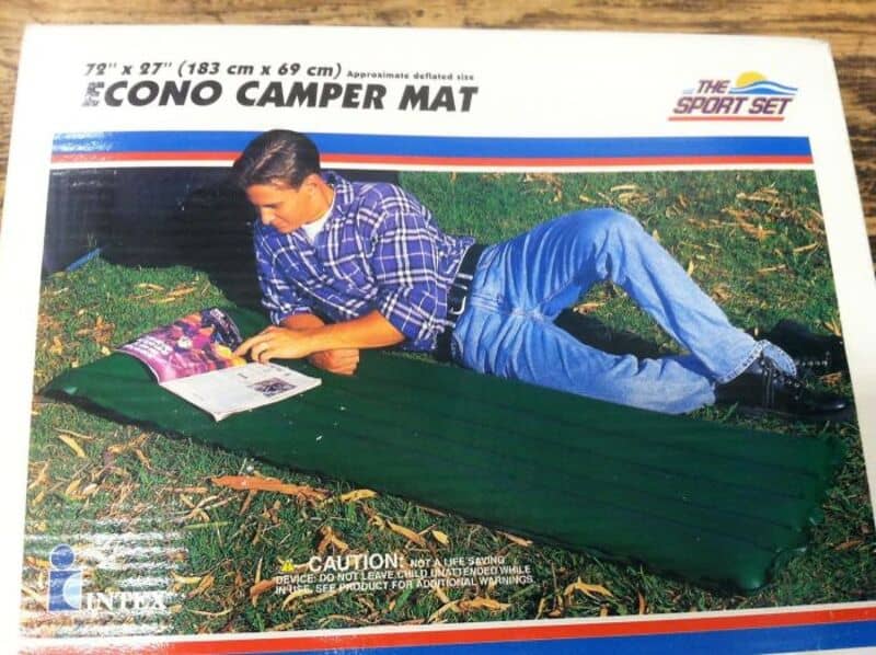 Young man reading on a green camper mat outdoors, product label visible.