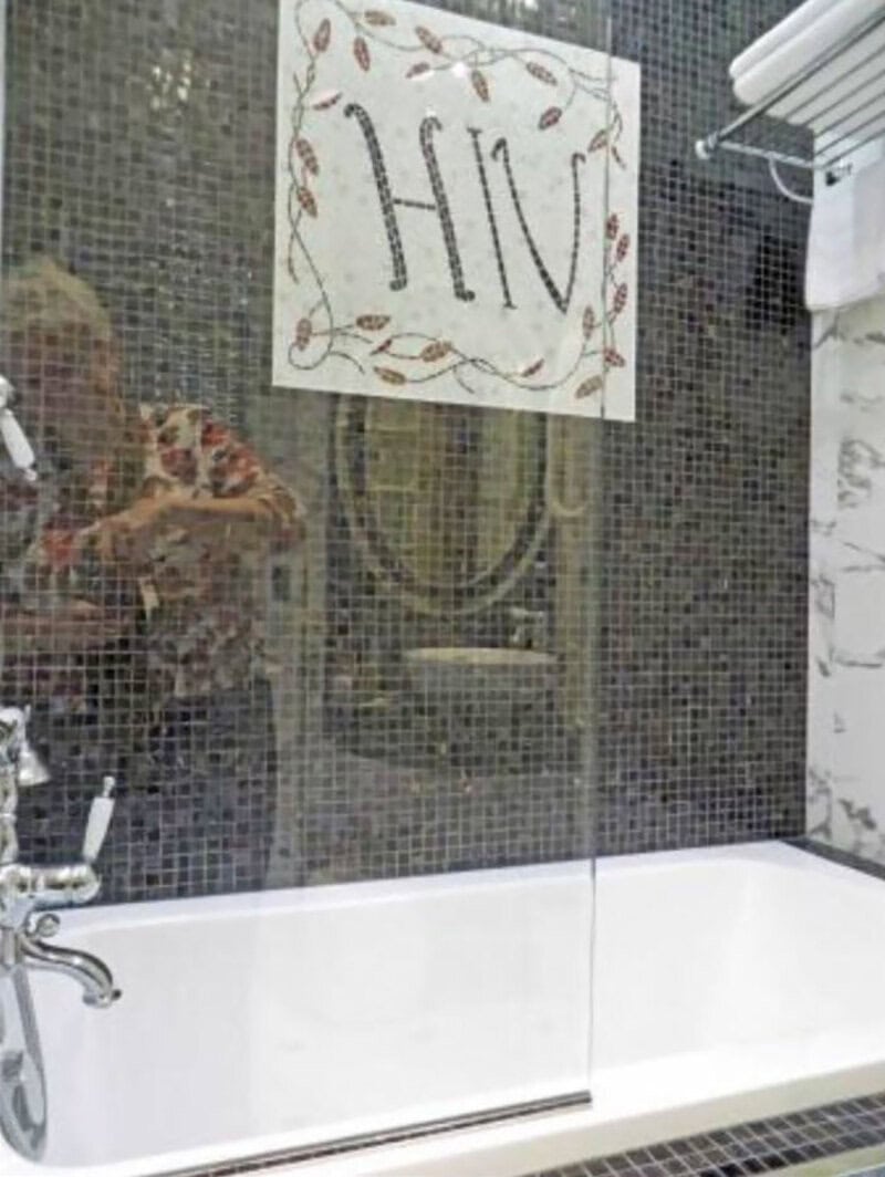 Mirror with a sign that reads 'HIV' in a bathroom with mosaic tiles.
