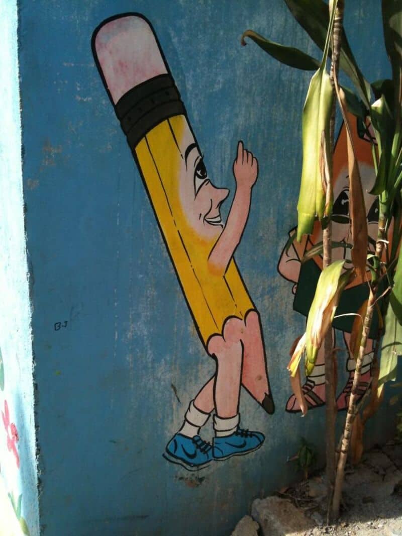 Cartoon pencil character giving a thumbs up on a blue wall.
