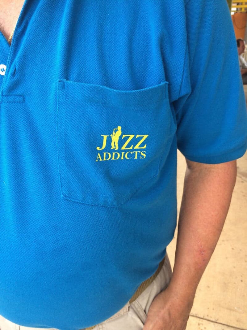 Blue shirt with a pocket and yellow text that says 'JIZZ ADDICTS'.