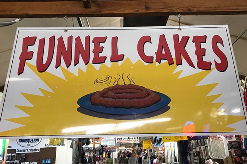 Funnel Cakes sign with a picture of a funnel cake on a blue plate.