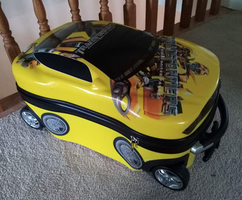 Child's yellow suitcase with a Cars movie design and black zipper, on carpeted floor.