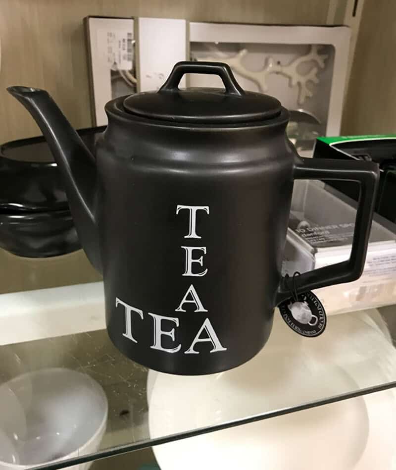 Black teapot with 'TEA' written vertically and horizontally in white letters.