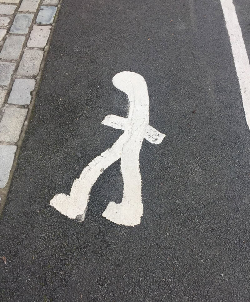 Humorous pedestrian symbol on the road with a missing head and a walking stick.