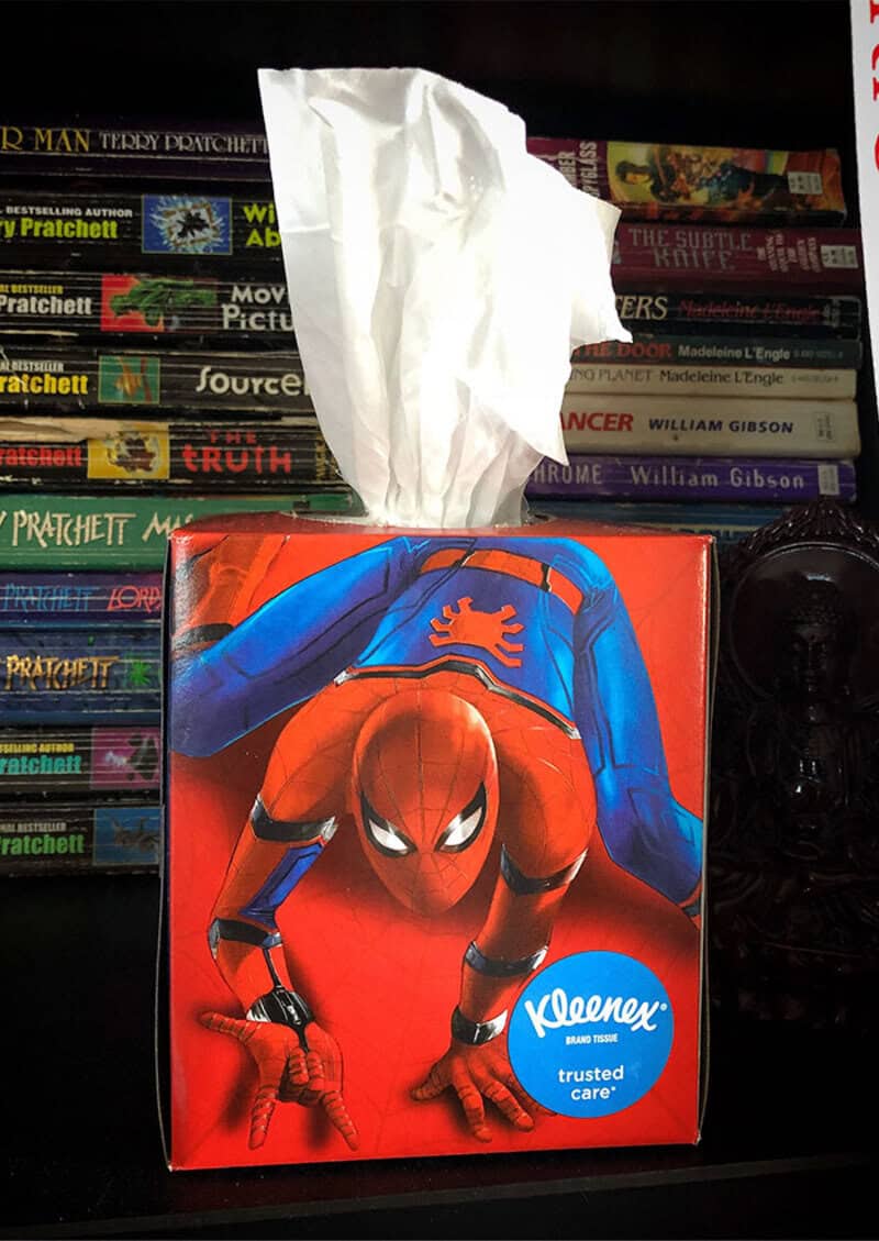 Spider-Man tissue box with tissue pulled out, in front of a bookshelf.