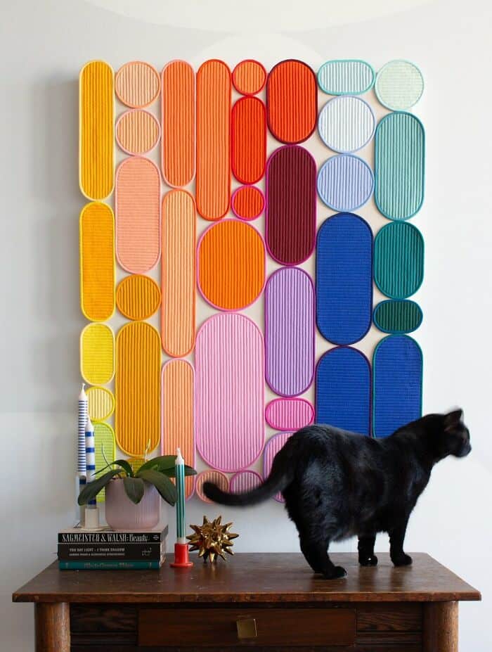 Colorful abstract wall art with various oval and circular shapes, black cat on wooden table.