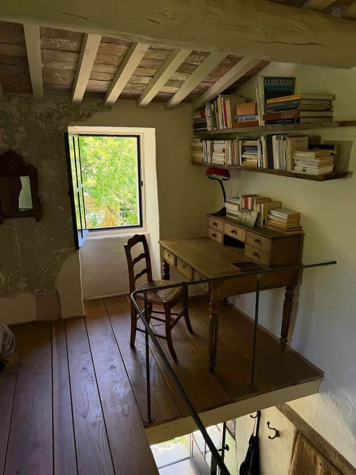 Cozy attic reading nook with a small window, wooden desk, and shelves filled with books.