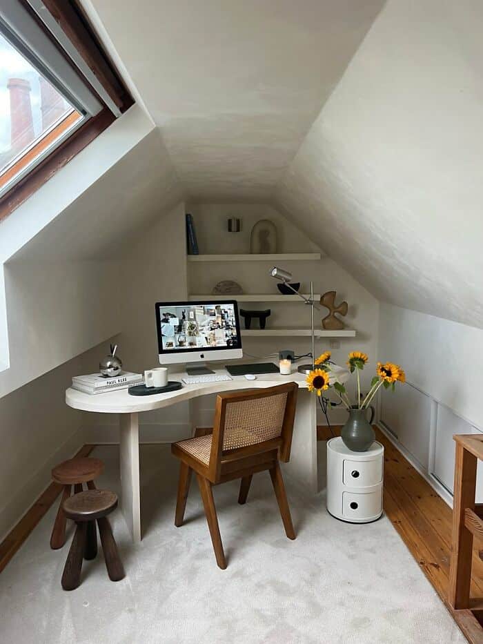 Cozy attic workspace with desk, chair, sunflower vase, and shelves under sloped ceiling.