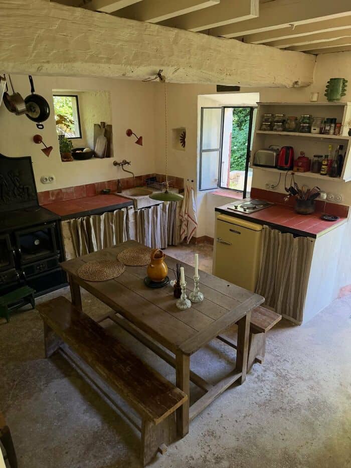 Cozy rustic kitchen with open window, wooden table, and vintage decor.