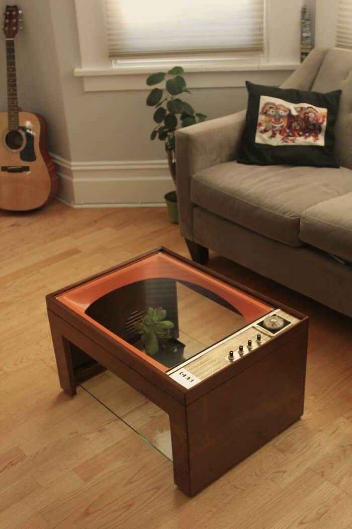 Modern wooden coffee table with glass top and plant in living room.
