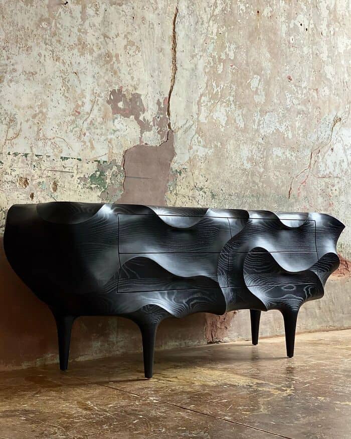 Black modern sculptural sideboard with curved lines and textured surface, standing on four tapered l.