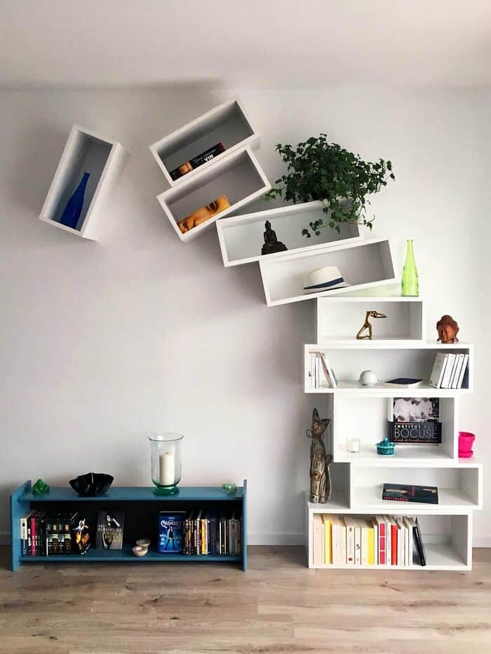 Modern white zigzag wall shelves with books and decorative items in a living room.