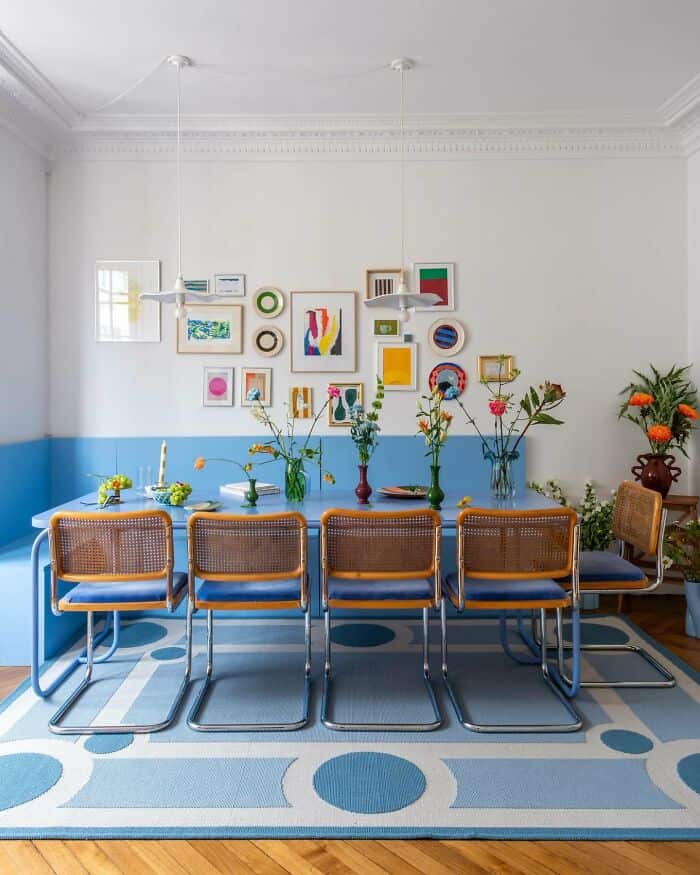 Modern dining room with colorful wall art and flower arrangements on a blue table.