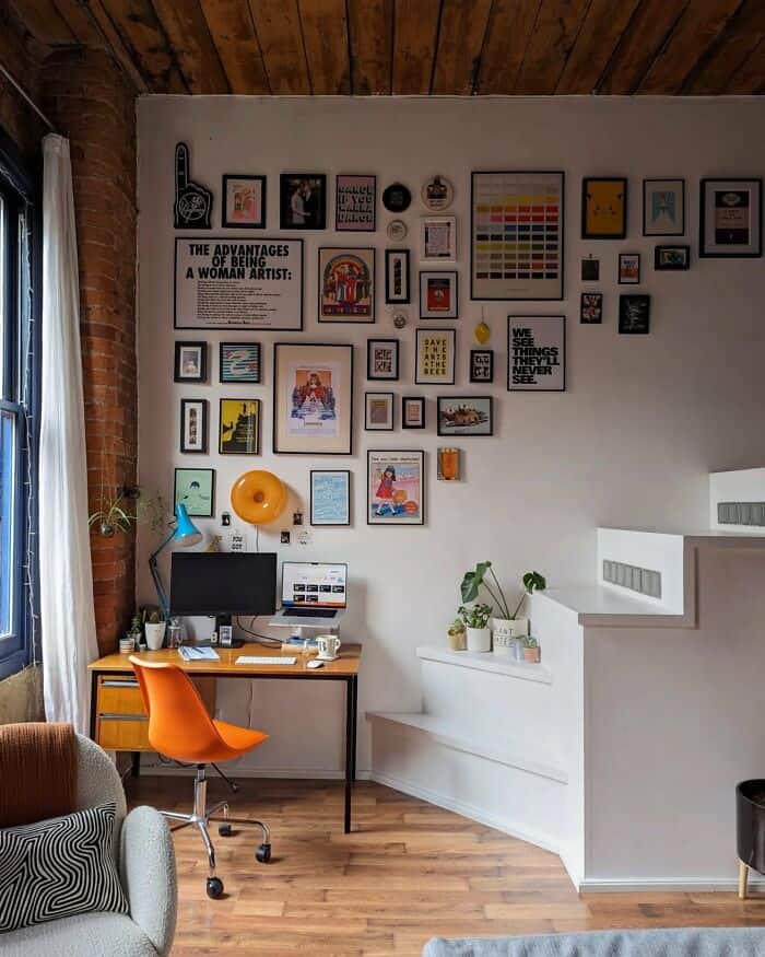 A colorful gallery wall with various framed artworks and posters in a modern home office.