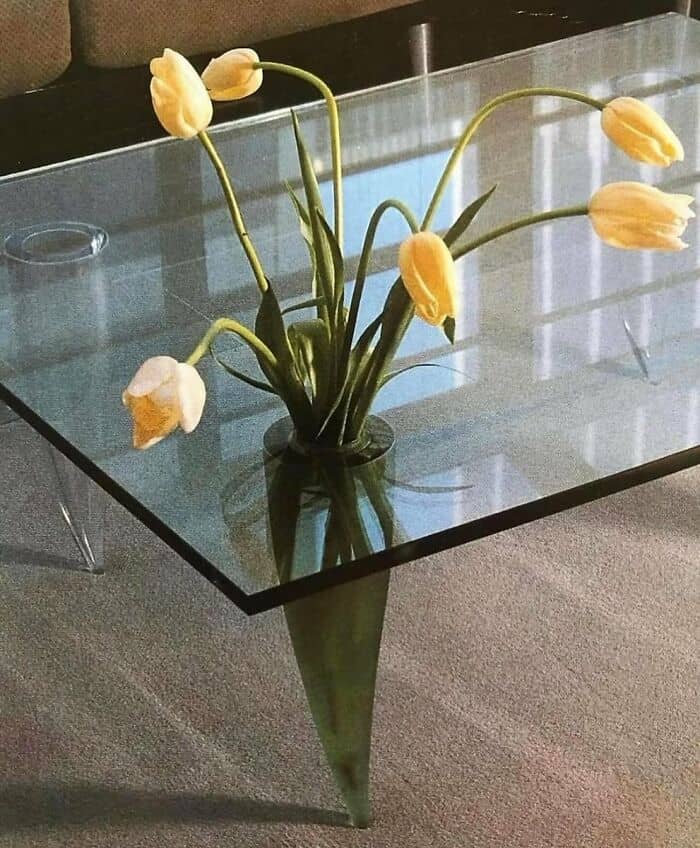 Glass table with a vase of yellow tulips on top.