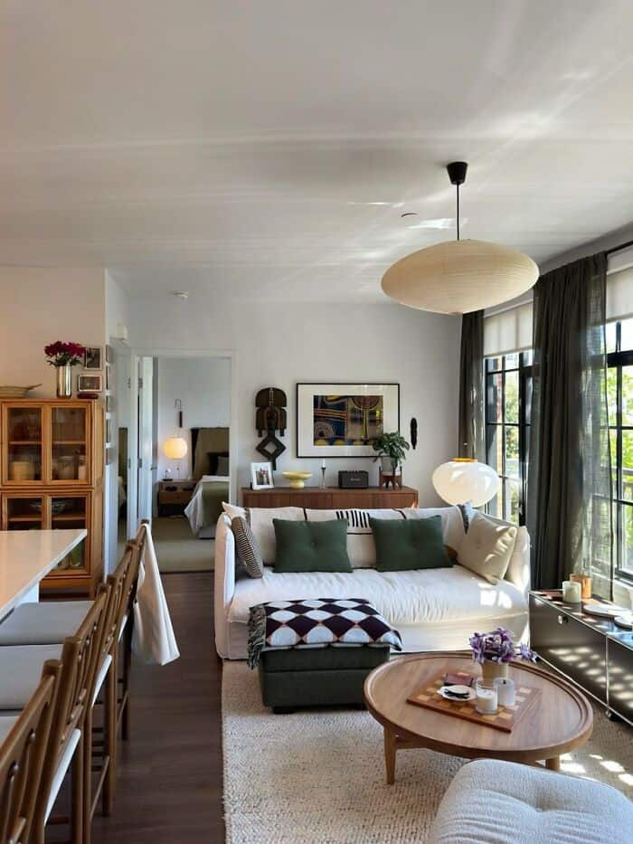 Bright living room with white sofa, green cushions, and large windows with black curtains.