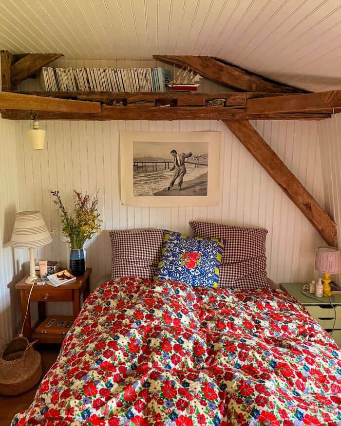 Cozy bedroom with floral bedspread, vintage decor, and wooden beams in an attic space.