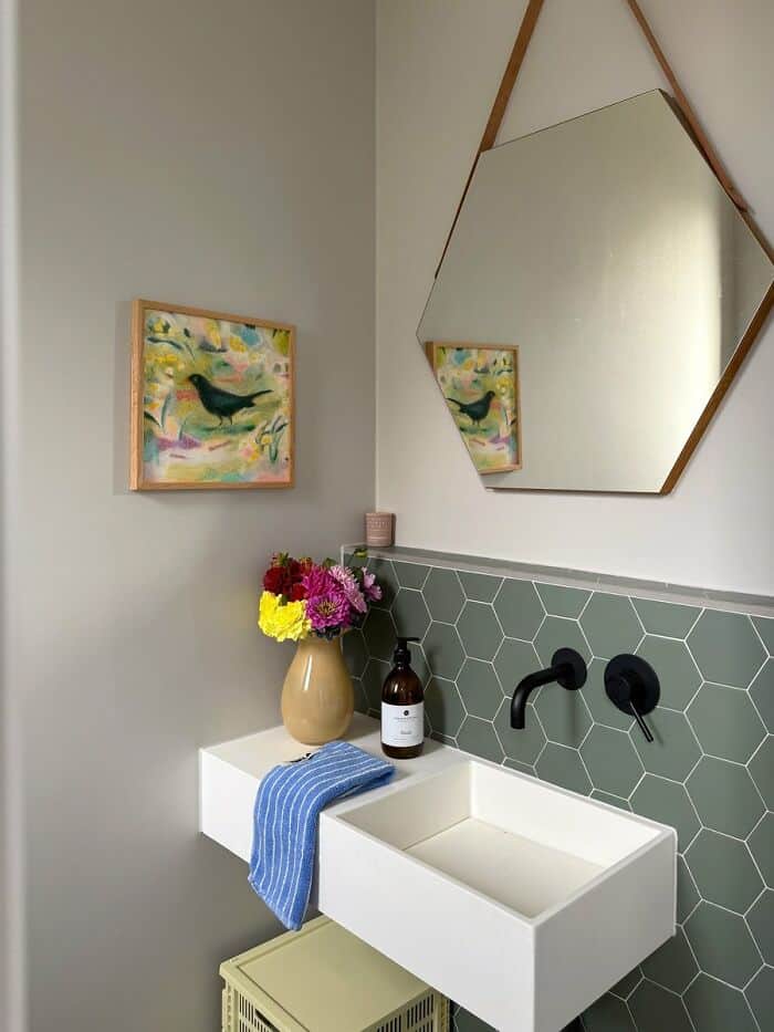 Modern bathroom with hex tile wall, mirror, and colorful artwork.