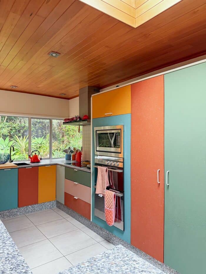 Bright colorful kitchen with orange, yellow, teal, and green cabinets, and a wooden ceiling.