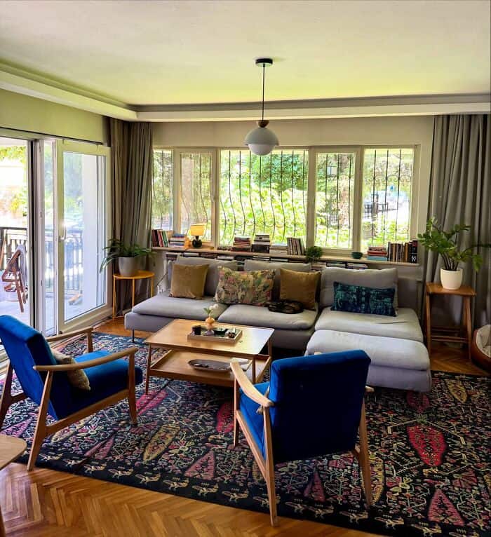 Cozy living room with large windows, colorful cushions, and a patterned rug.