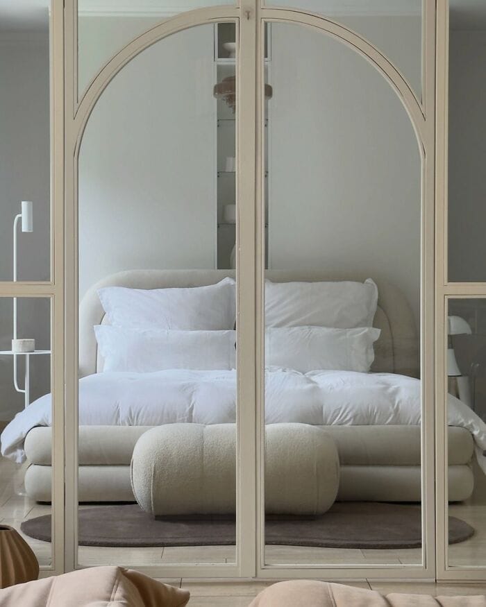 Elegant beige sofa reflected in a large mirror with an arched top and wooden frame.