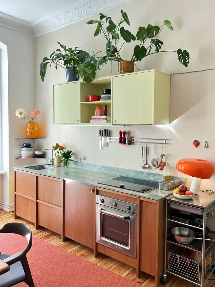 Bright kitchen with green cabinets, potted plants, and a small cart with kitchen essentials.