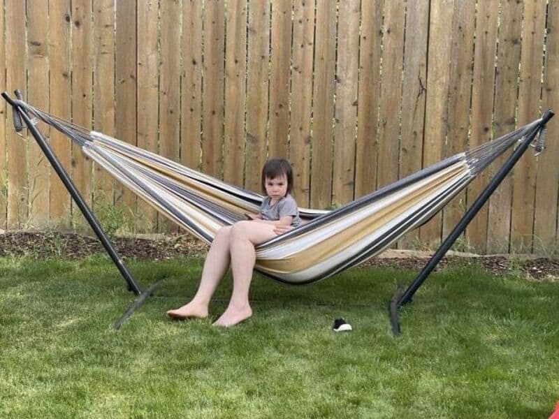 Child sitting in a hammock in a backyard with a wooden fence.