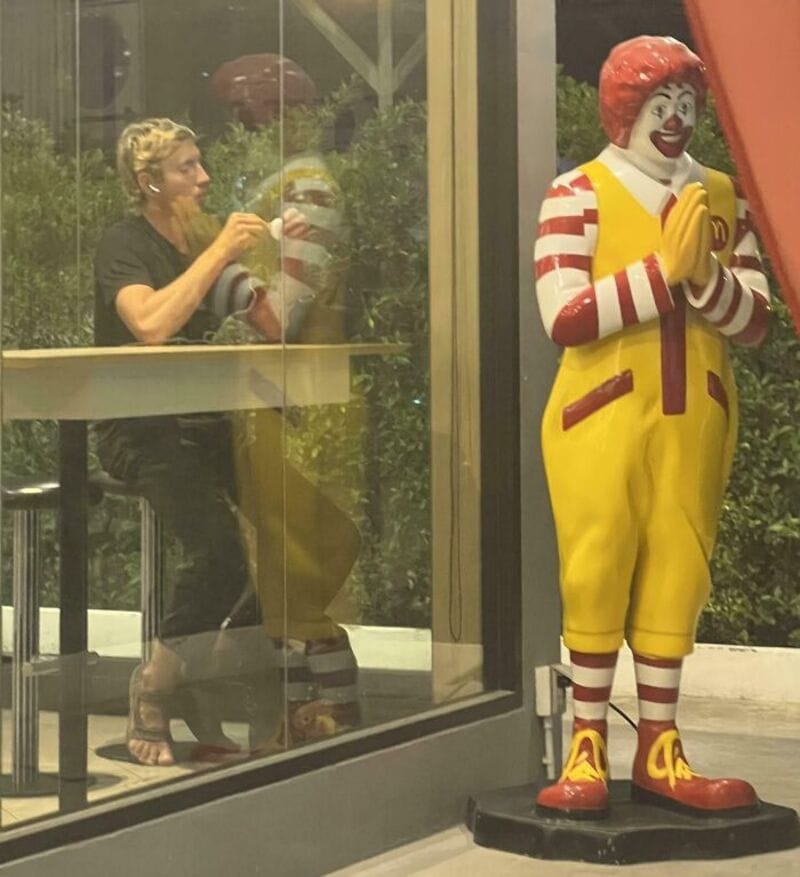 Person sitting at a table with a clown statue outside the window.