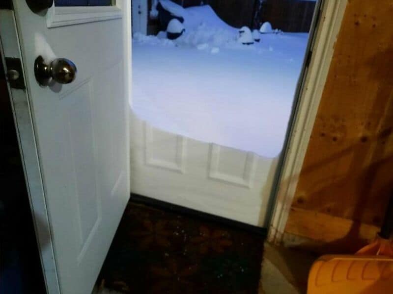 Open door showing snow-covered yard outside, inside wooden floor and door frame.