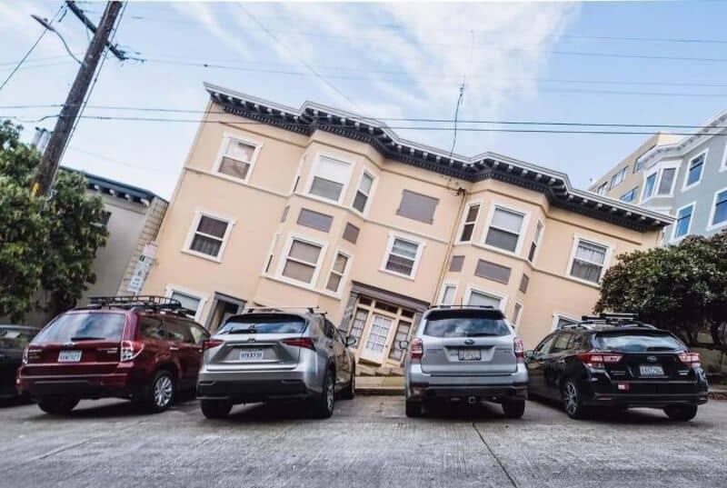 Upside-down house with cars parked in front, under a clear sky.