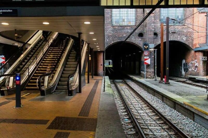 Escalators in a subway station next to train tracks and a brick tunnel.