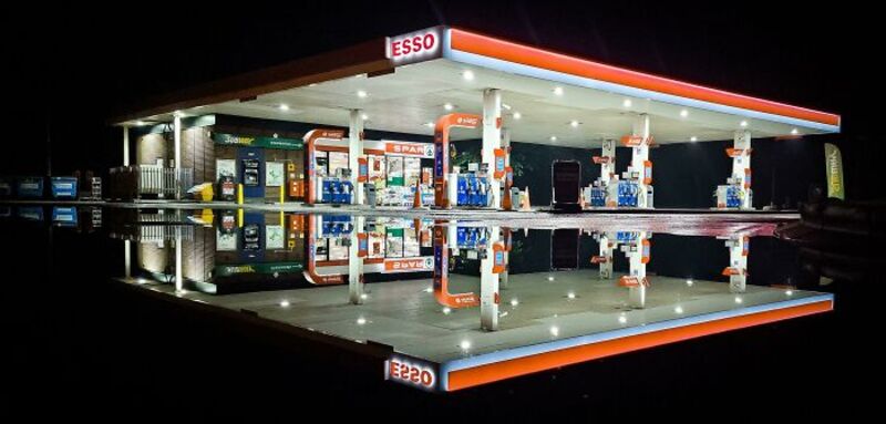 Reflections of a gas station at night with bright lights and fuel pumps.