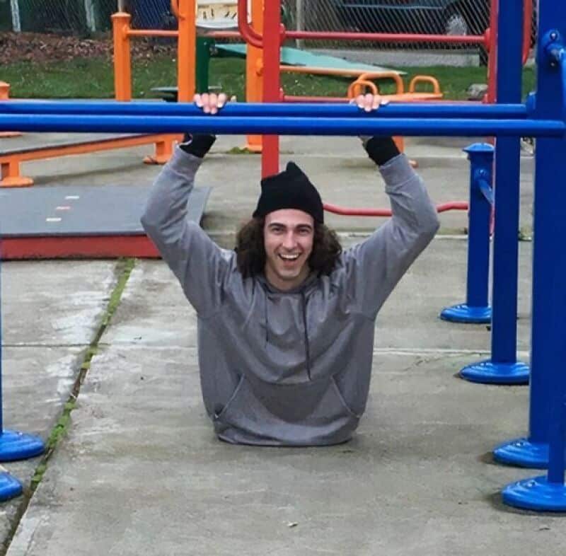 Person hanging upside down from playground bars, smiling, wearing a gray hoodie and black beanie.