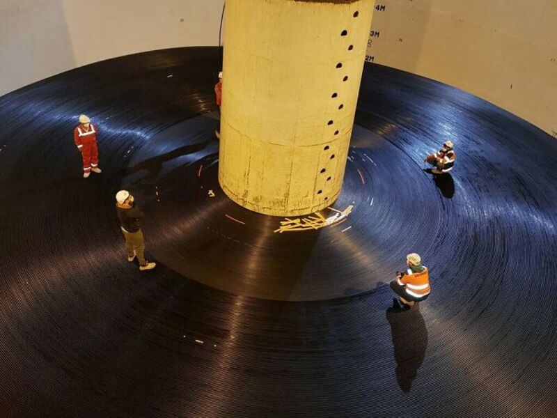 Workers inspect a large vinyl record with a yellow cylindrical object in the center.