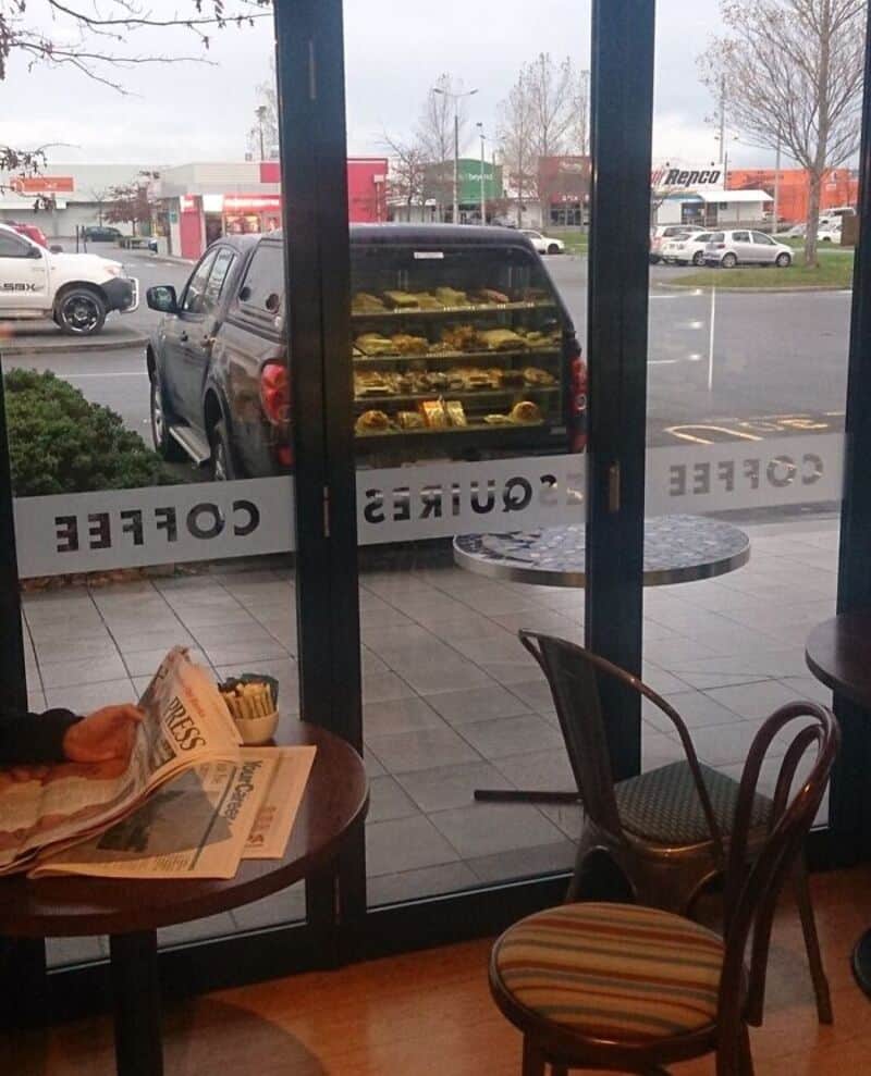 View of a bakery display case outside a coffee shop with a pickup truck in the background.