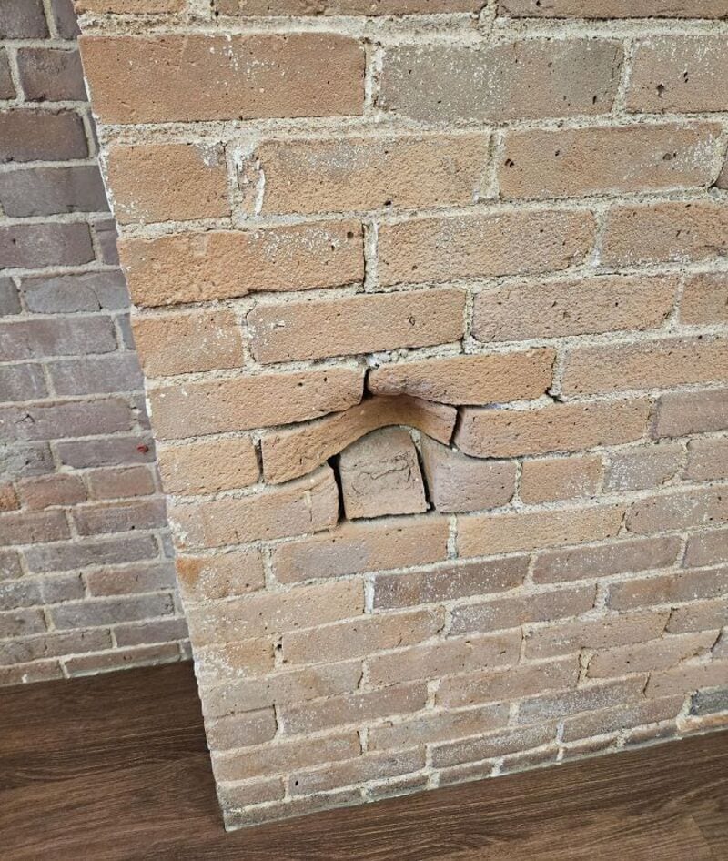 Brick wall with a large crack and a small piece of brick missing.