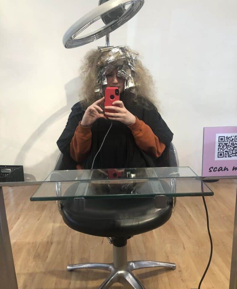 Person with foil on head taking a selfie in a salon mirror.