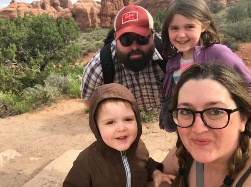 Family of four taking a selfie outdoors with red rock formations in the background.