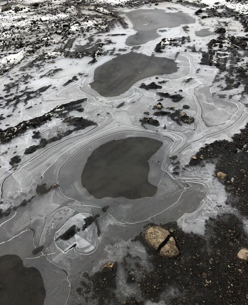 Two puddles on the ground with cracked ice and rocks.