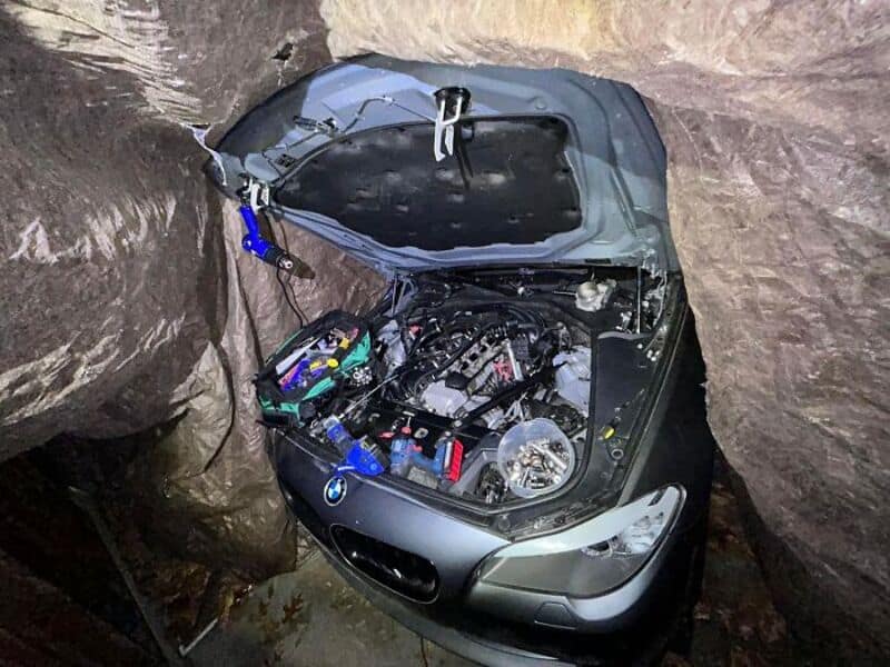 Car trapped between rocks with open hood in a narrow space.
