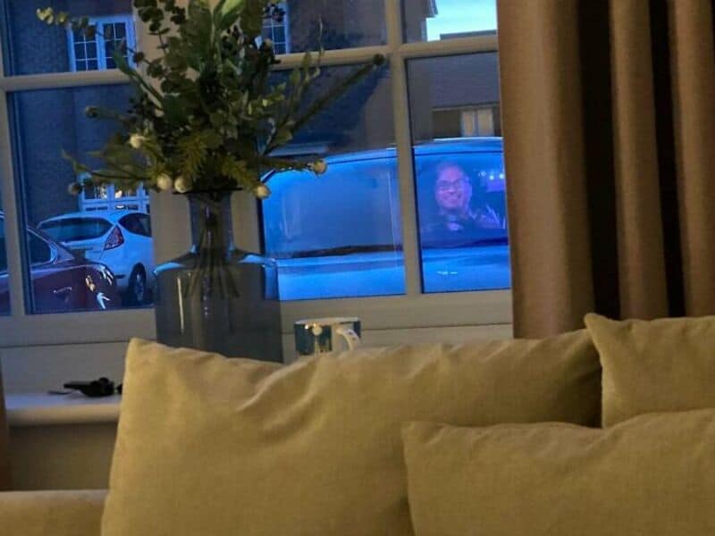 Person looking out window at night with a blue reflection on the glass.