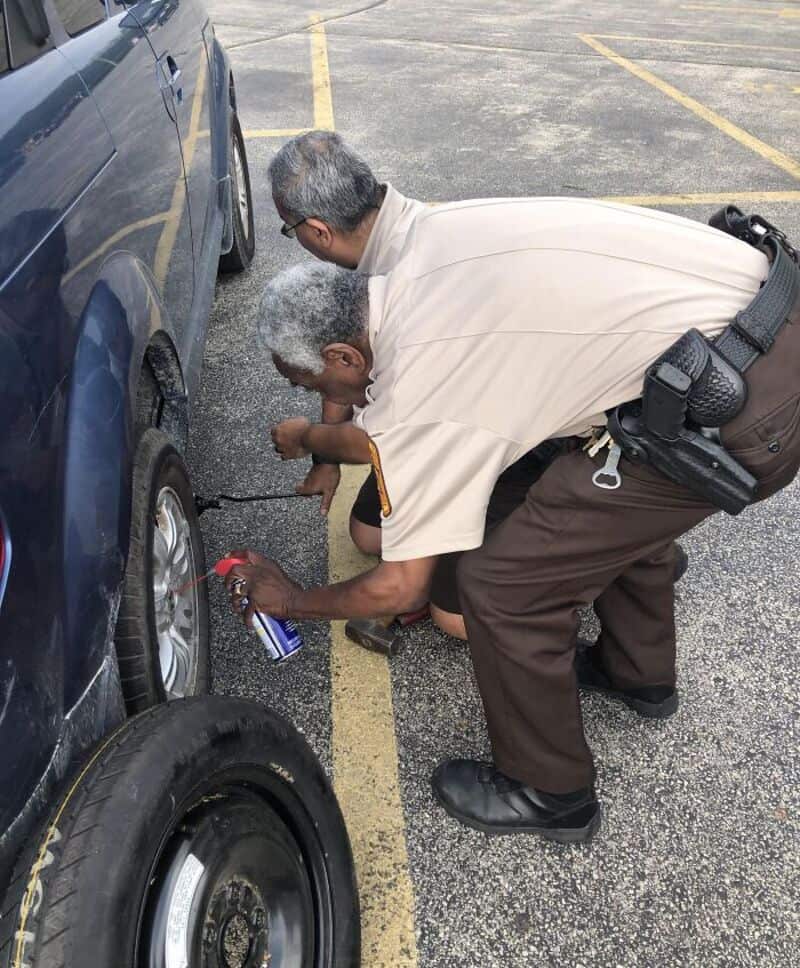Two police officers inspecting a car tire in a parking lot.