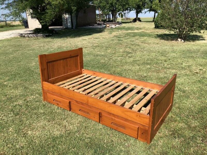 Wooden bed frame with storage drawers on a grassy lawn.