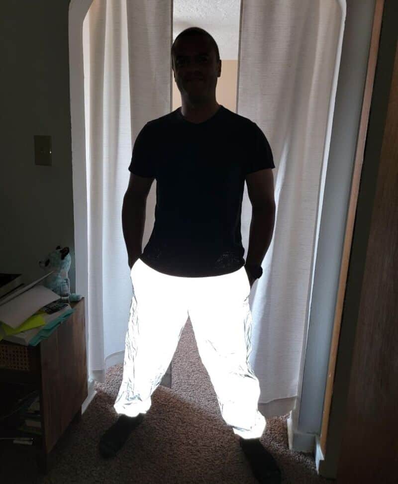 Person standing in front of curtains, wearing dark shirt and reflective pants.