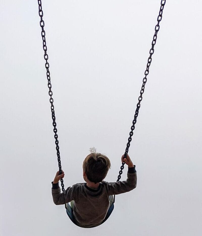 Child on a swing with chains against a plain sky background.