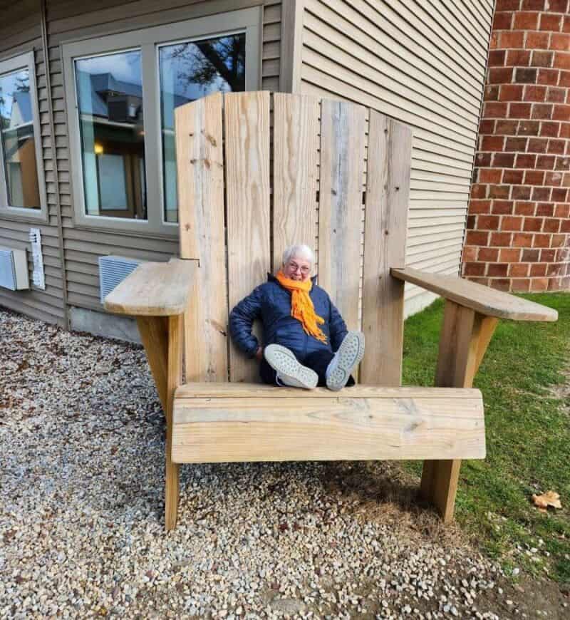 Child sitting on a giant wooden chair outside a house.