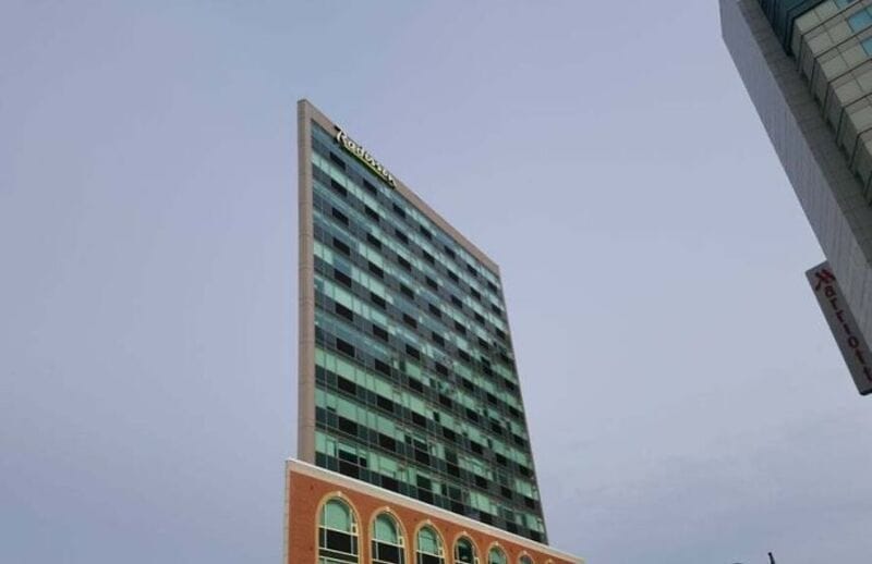 Tall building with a mix of glass windows and brick architecture, under a cloudy sky.