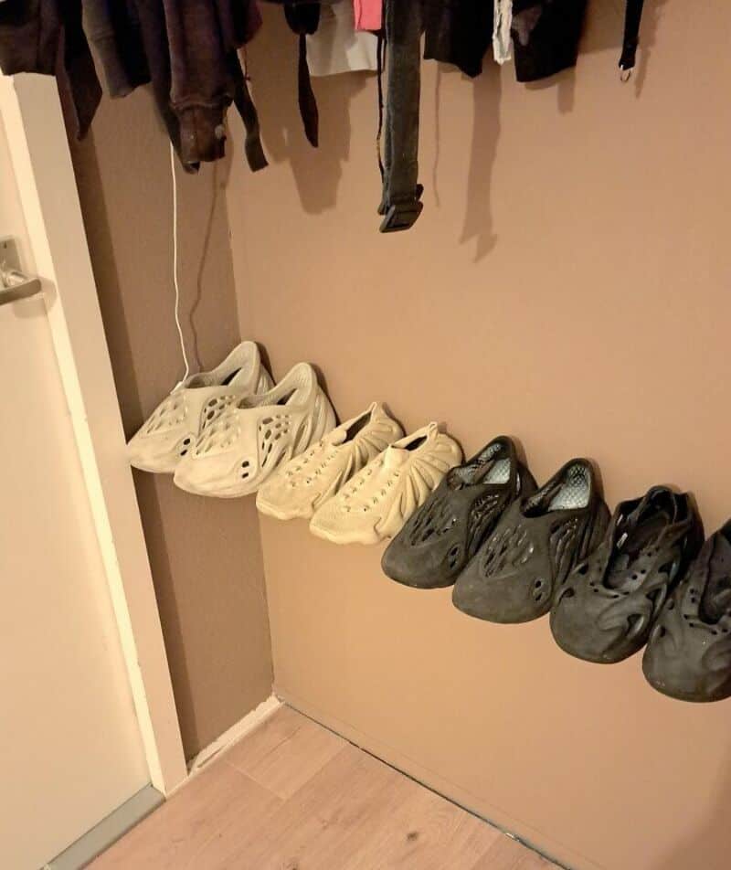 Six pairs of shoes on a ledge under hanging clothes in a closet.